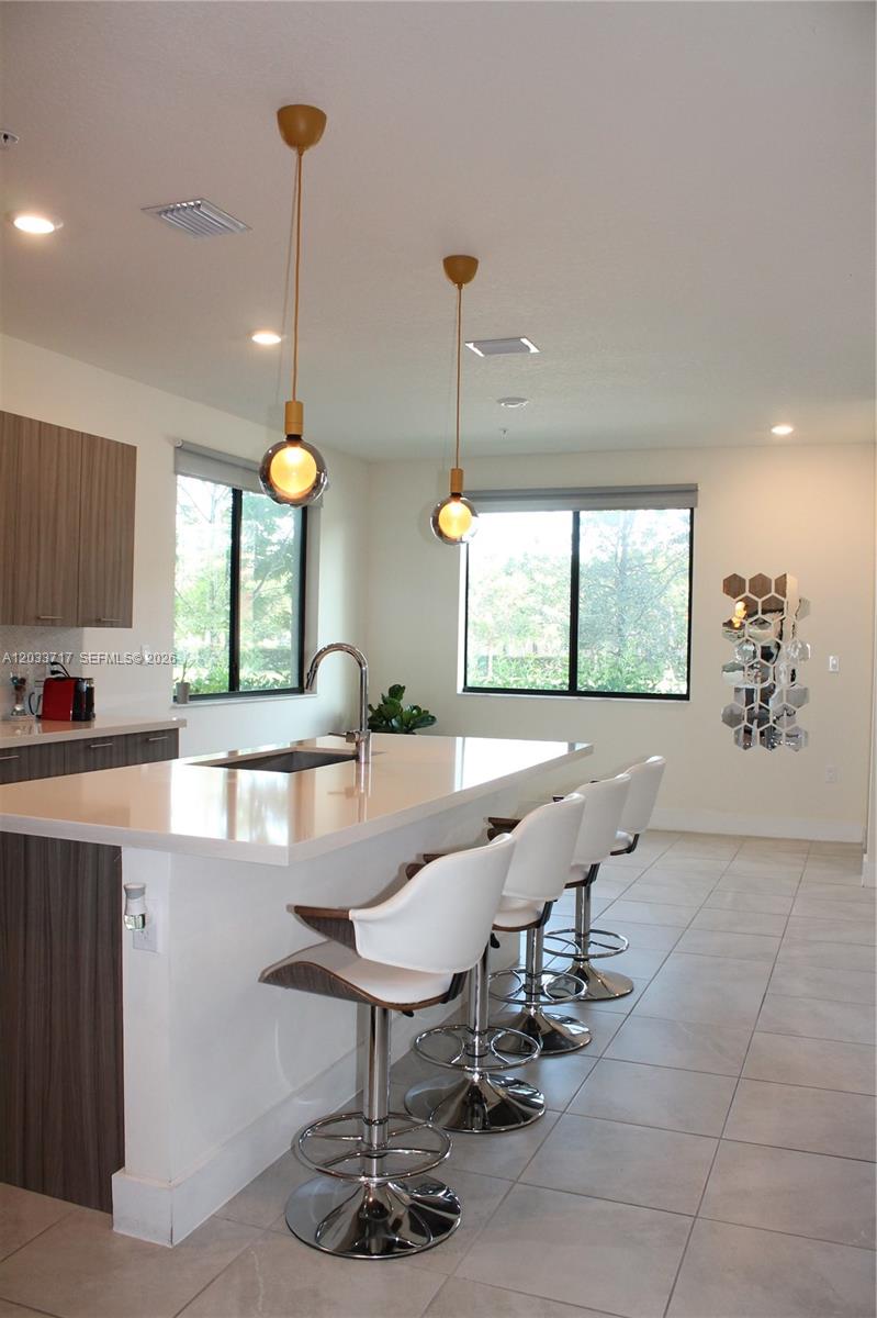 A modern kitchen features a white island with bar stools and two pendant lights — 8265 NW 41 ST # 110, Doral FL 33166, DORAL, FL