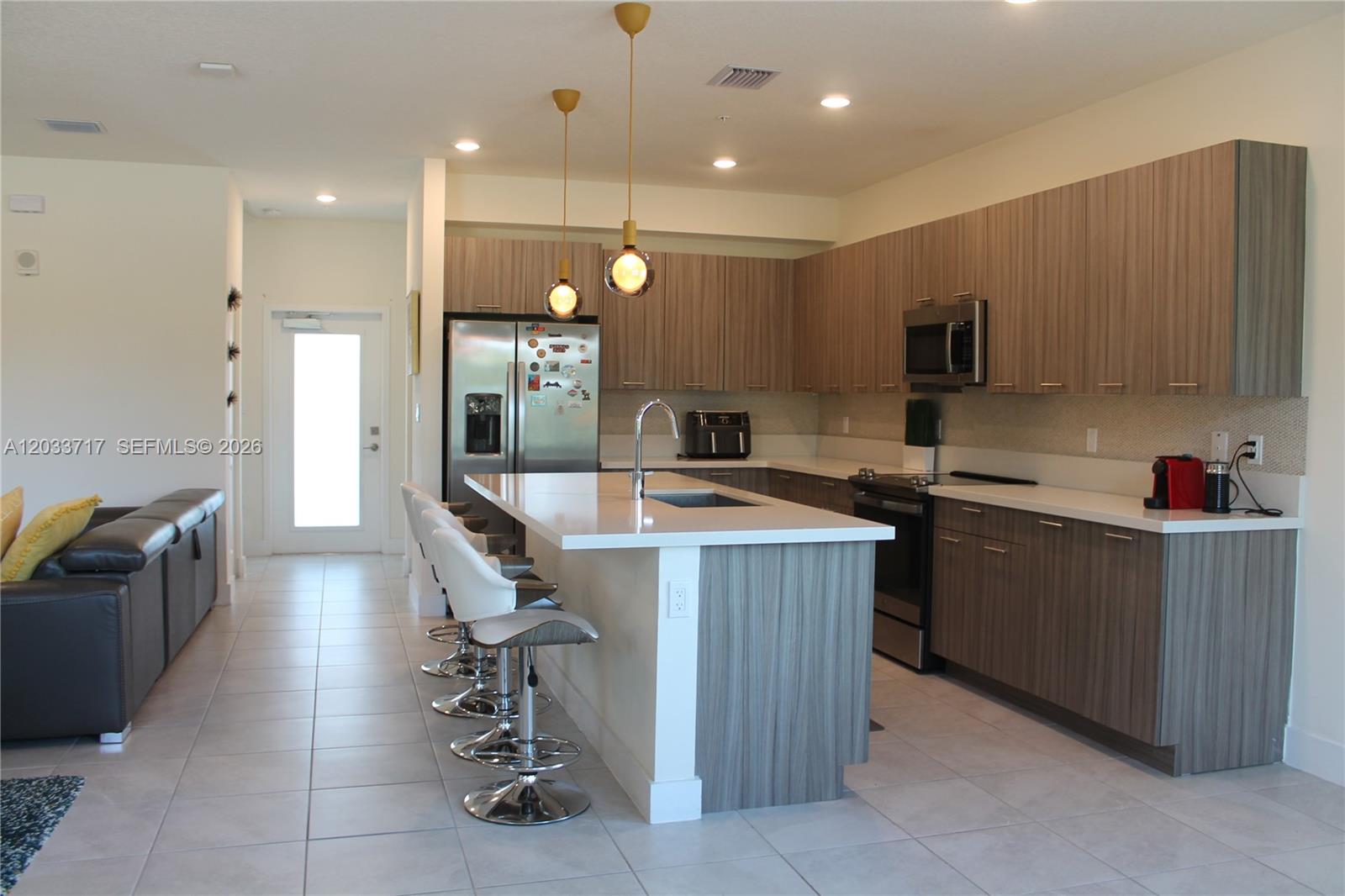 A modern kitchen features wood-grain cabinets, a white quartz island, and stainless steel appliances — 8265 NW 41 ST # 110, Doral FL 33166, DORAL, FL