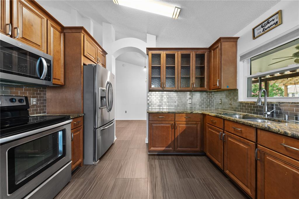 A kitchen with wood cabinets, stainless steel appliances, granite countertops, and a gray tile backsplash — 308 SILVER PINE DRIVE, LAKE MARY, FL
