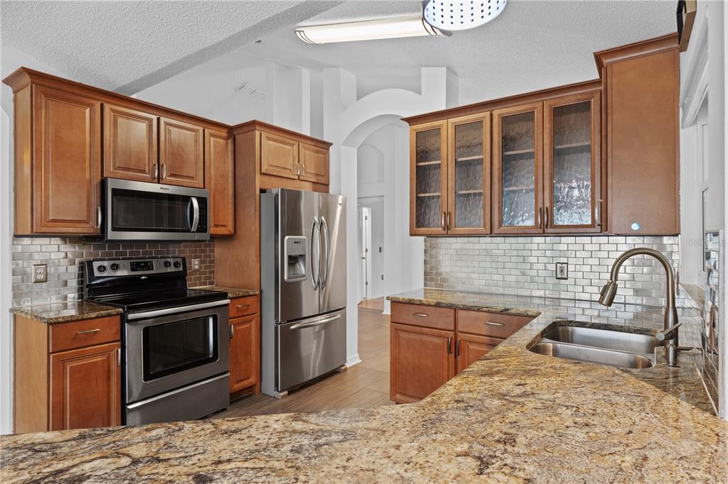 A kitchen with wood cabinets, stainless steel appliances, granite countertops, and a subway tile backsplash — 308 SILVER PINE DRIVE, LAKE MARY, FL