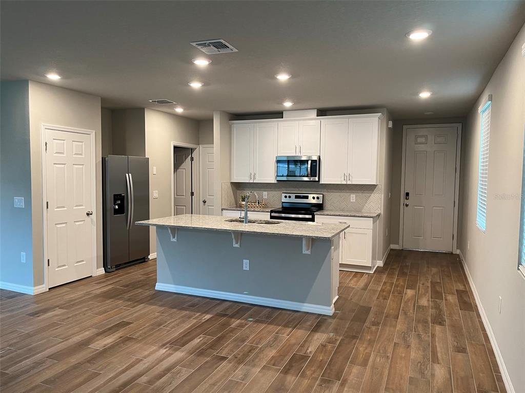 A kitchen with white cabinets, granite countertops, a center island, and wood-look tile flooring — 437 LEGACY LOOP, DAVENPORT, FL