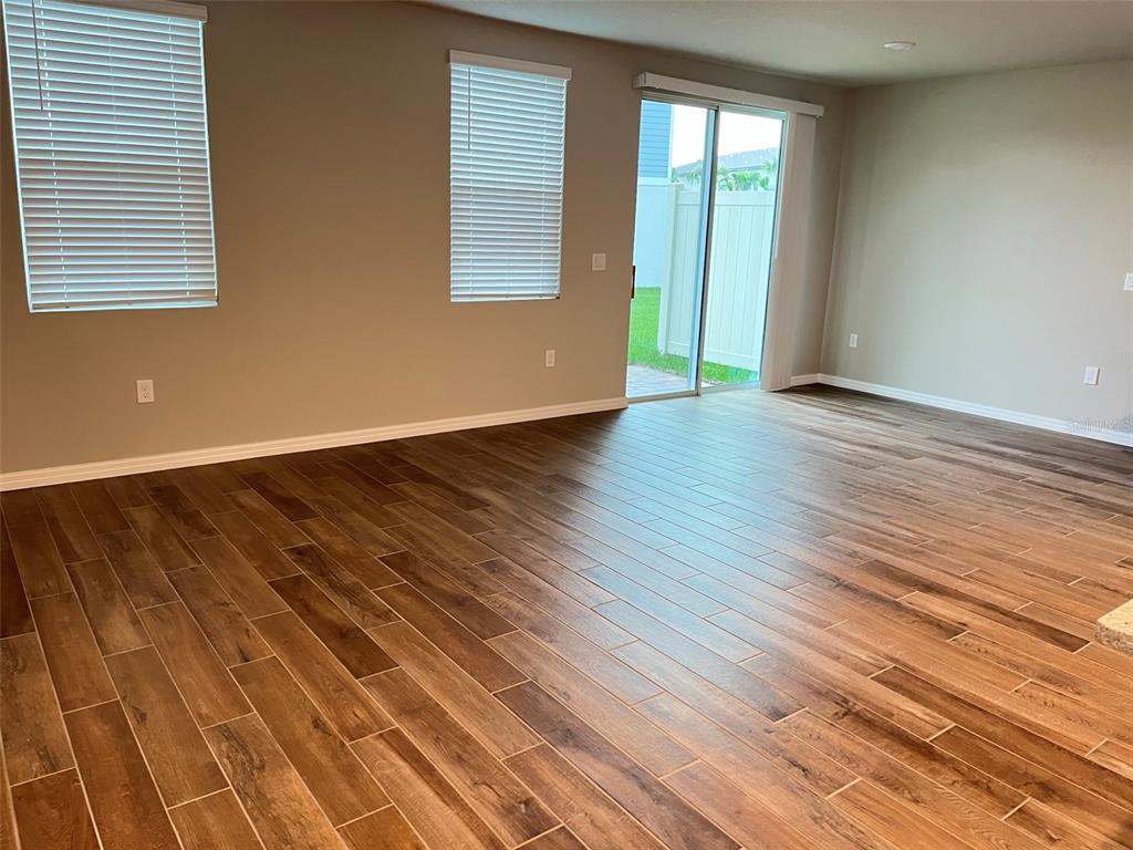 An empty room features wood-look tile flooring, two windows with blinds, and a sliding glass door — 437 LEGACY LOOP, DAVENPORT, FL