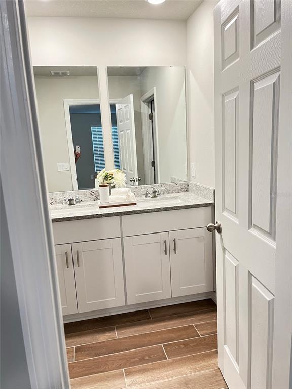 A bathroom features a double vanity with white cabinets, a stone countertop, and wood-look flooring — 437 LEGACY LOOP, DAVENPORT, FL