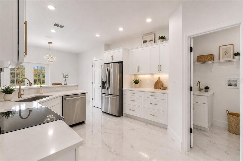 A modern white kitchen features stainless steel appliances, marble-look tile flooring, and an adjacent pantry — 17545 GLENDA DRIVE, SPRING HILL, FL