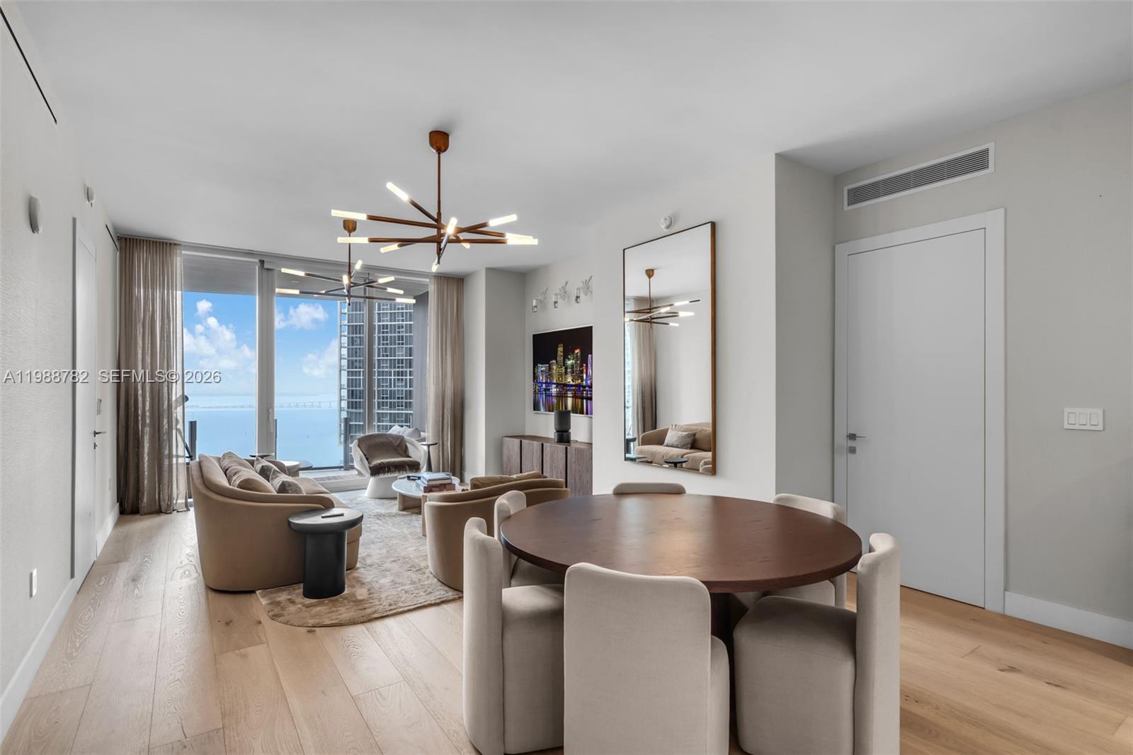 A modern living and dining area features light wood floors, floor-to-ceiling windows, and ocean views — 300 Biscayne Boulevard Way # 2605W, Miami FL 33131, MIAMI, FL