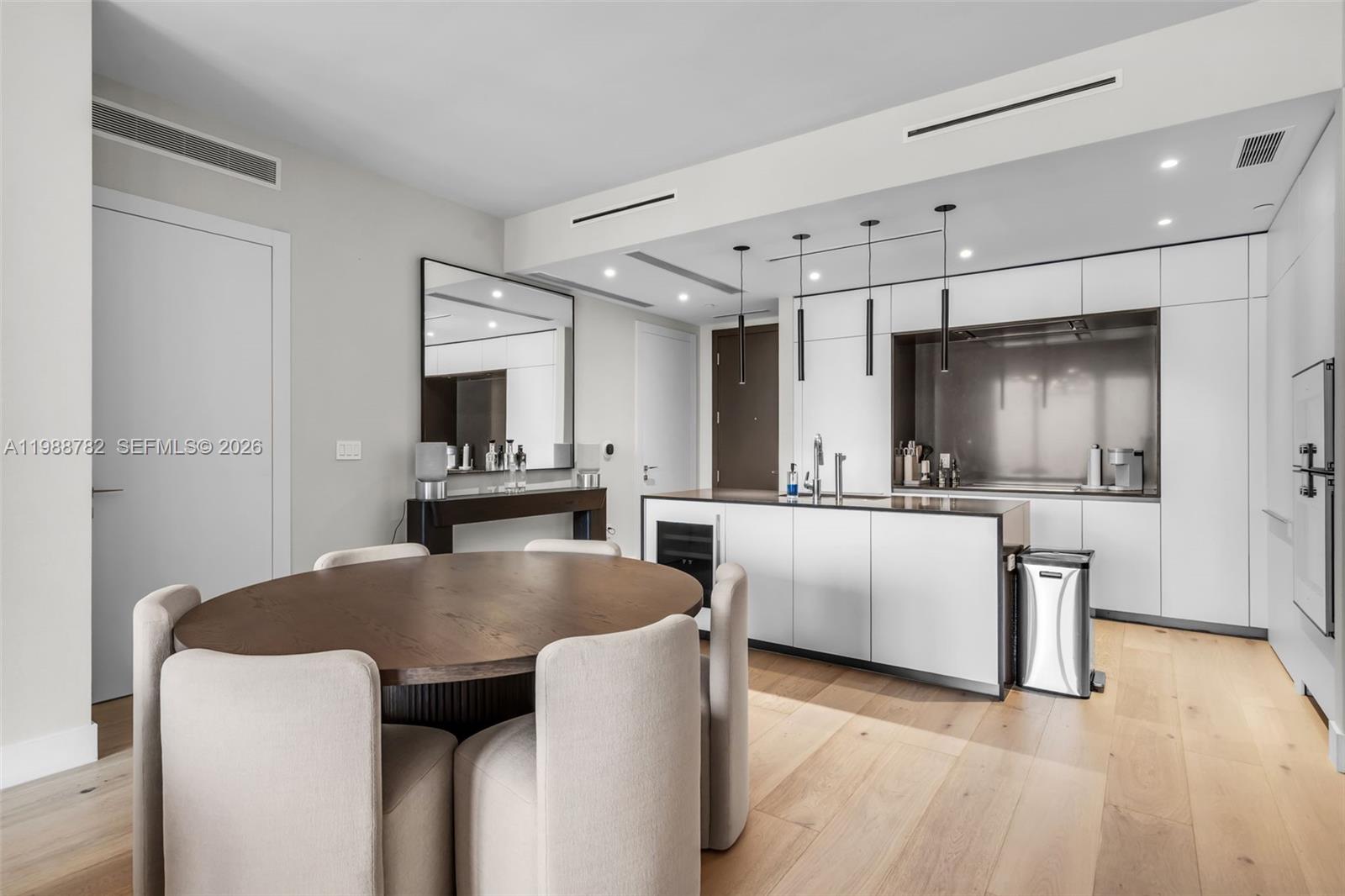A modern kitchen features white cabinetry, a central island, and a round wooden dining table — 300 Biscayne Boulevard Way # 2605W, Miami FL 33131, MIAMI, FL