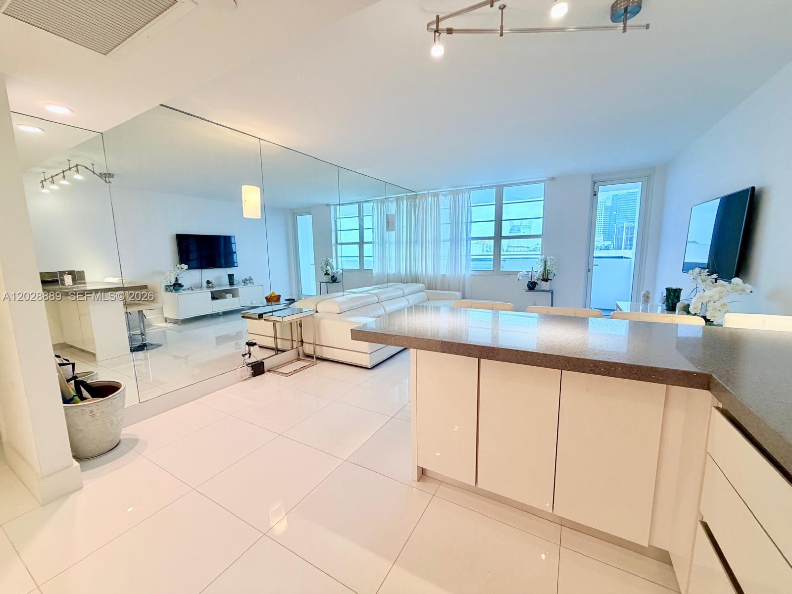 A modern open-concept living area features white tile floors, a mirrored wall, and kitchen island — 100 Lincoln Rd # 1504, Miami Beach FL 33139, MIAMI BEACH, FL