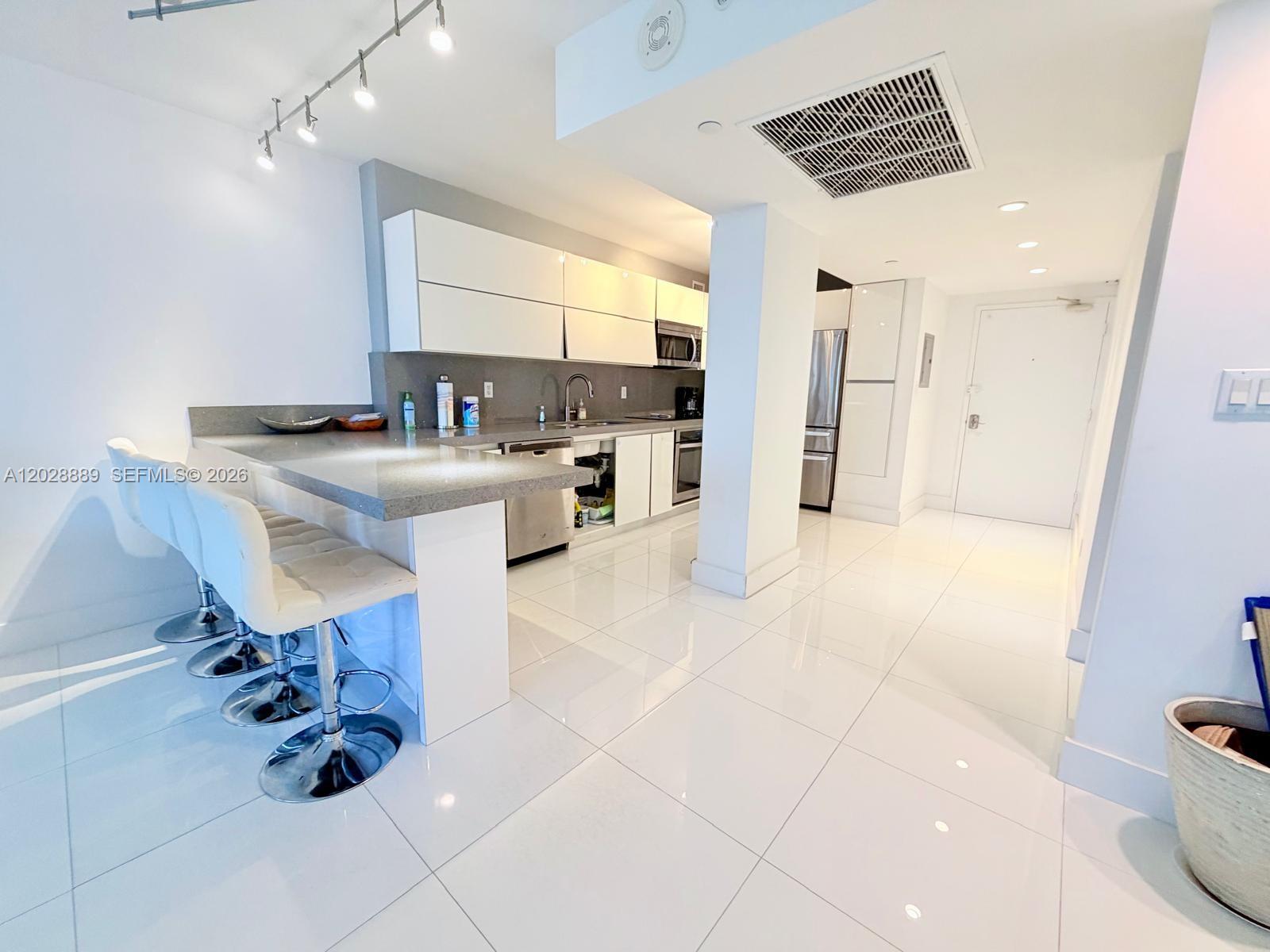 A modern kitchen features white cabinetry, a gray stone countertop, and white tile flooring — 100 Lincoln Rd # 1504, Miami Beach FL 33139, MIAMI BEACH, FL
