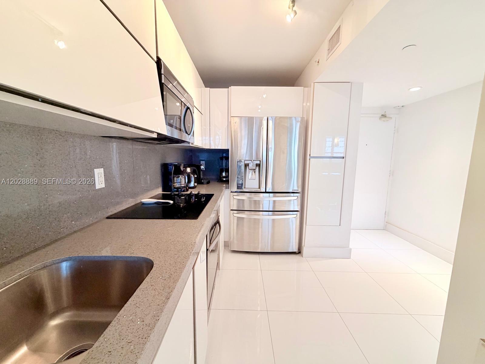 A modern kitchen features white cabinets, stainless steel appliances, and gray stone countertops — 100 Lincoln Rd # 1504, Miami Beach FL 33139, MIAMI BEACH, FL