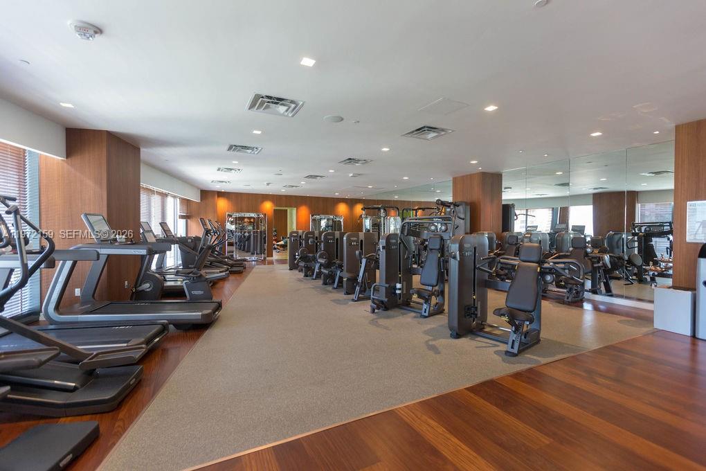 A modern fitness center features rows of exercise machines, wood flooring, and mirrored walls — 1300 S Miami Ave # 2006, Miami FL 33130, MIAMI, FL