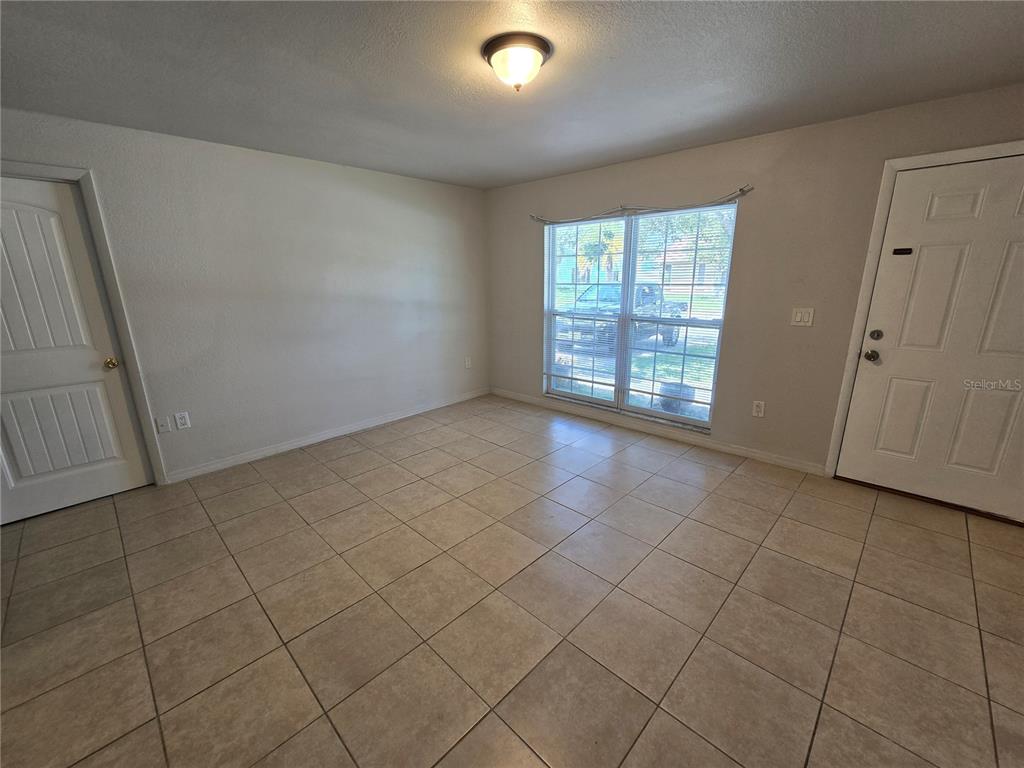 An empty room features beige tile flooring, white walls, a window, and a white door — 3406 MURROW STREET, NEW PORT RICHEY, FL