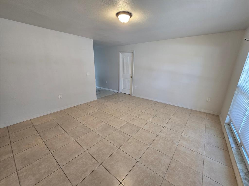 An empty room features beige tile flooring, white walls, a ceiling light, and a door — 3406 MURROW STREET, NEW PORT RICHEY, FL