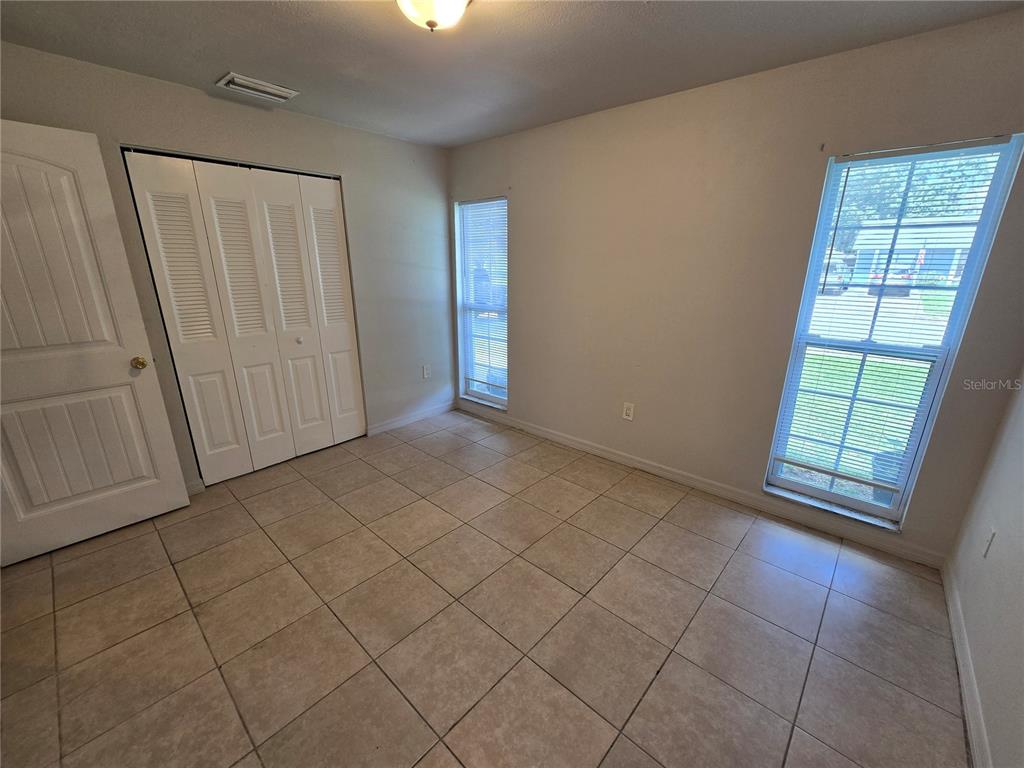 An empty room features beige tile flooring, white walls, a closet, and two windows — 3406 MURROW STREET, NEW PORT RICHEY, FL