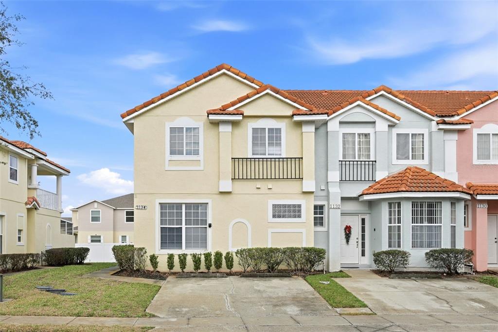 A two-story townhouse with a beige stucco exterior, a tiled roof, and a small balcony — 1134 S BEACH CIRCLE, KISSIMMEE, FL