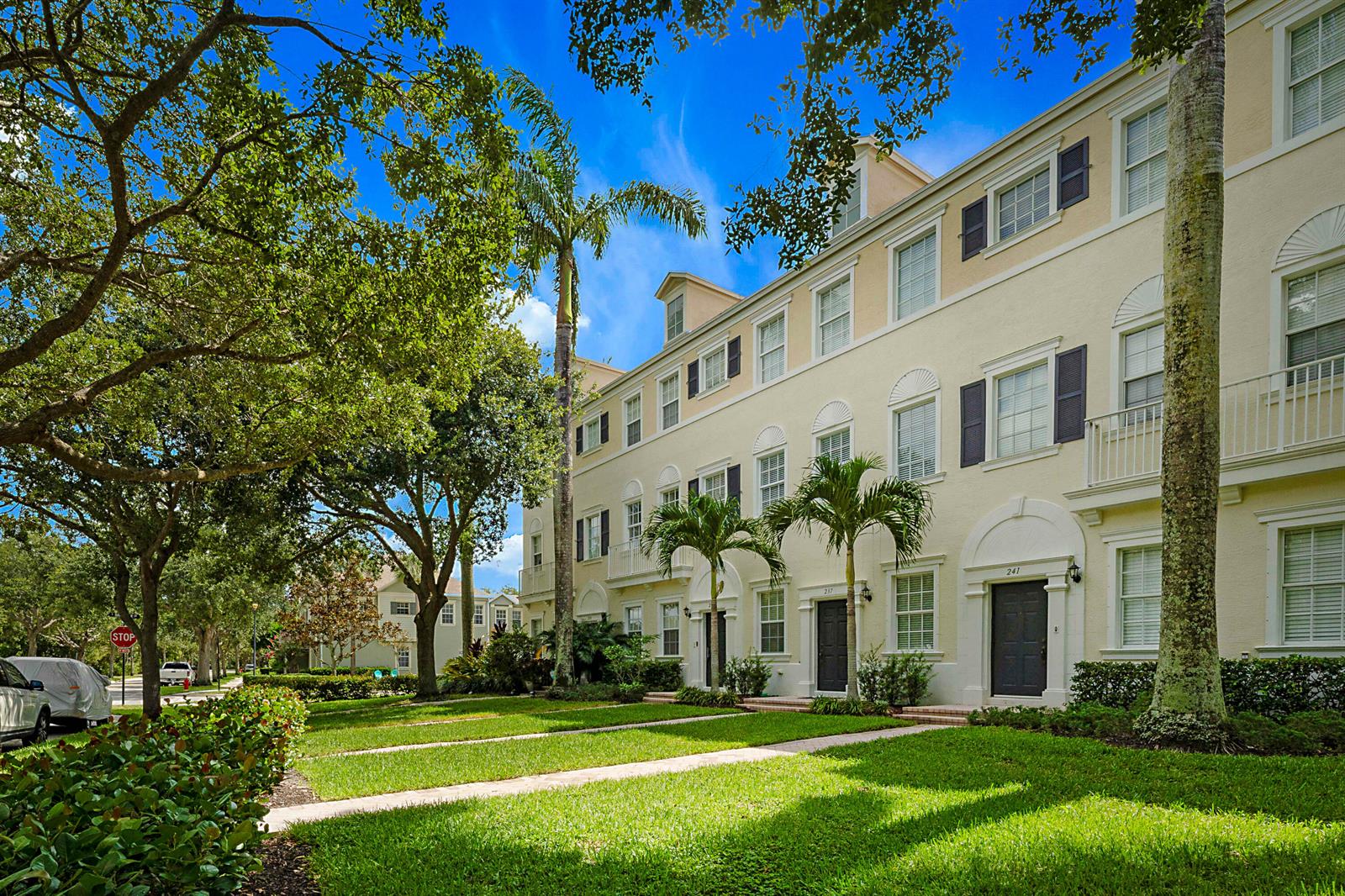 A three-story townhouse with a light-colored facade, dark shutters, and a front lawn — 241 E Thatch Palm Circle, Jupiter FL 33458, JUPITER, FL