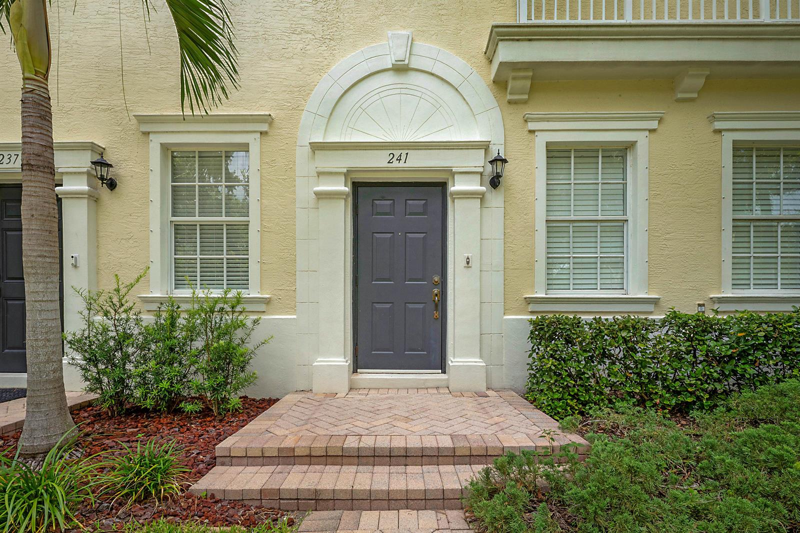 A front entrance with a gray door, arched trim, and brick steps on a yellow building — 241 E Thatch Palm Circle, Jupiter FL 33458, JUPITER, FL