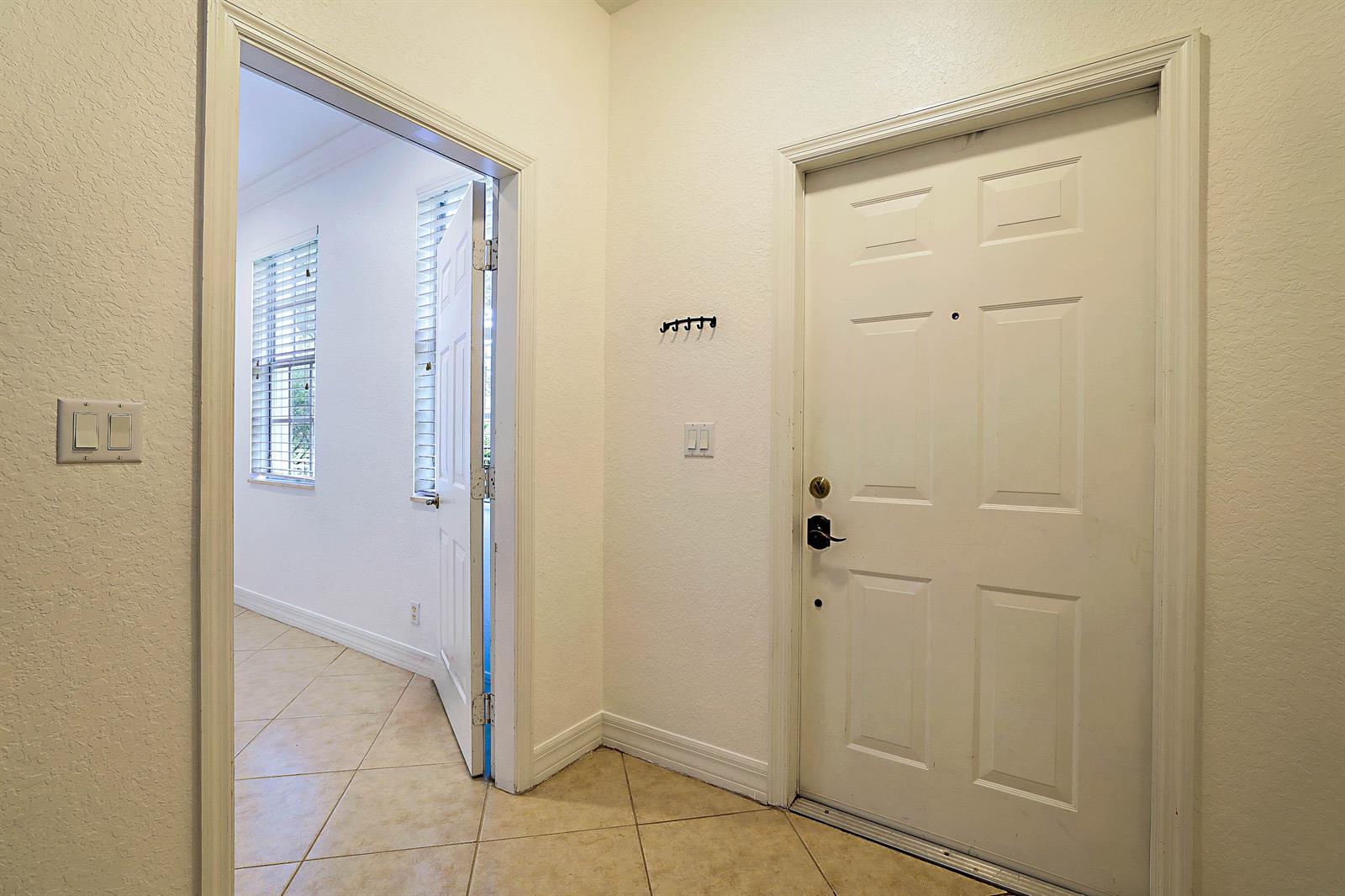 An entryway features a white front door, tiled flooring, and a doorway leading to a room — 241 E Thatch Palm Circle, Jupiter FL 33458, JUPITER, FL