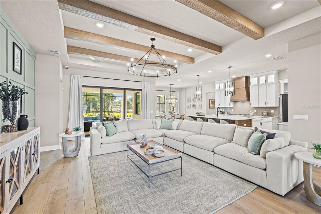 A spacious open-concept living room features wood ceiling beams, a large sectional, and kitchen views — 728 ESTATES BOULEVARD, TARPON SPRINGS, FL