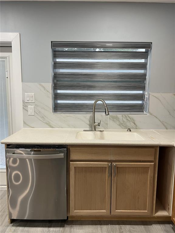A kitchen sink area features a stainless steel dishwasher, wood cabinets, and marble-look backsplash tile — 1746 8TH STREET, SARASOTA, FL