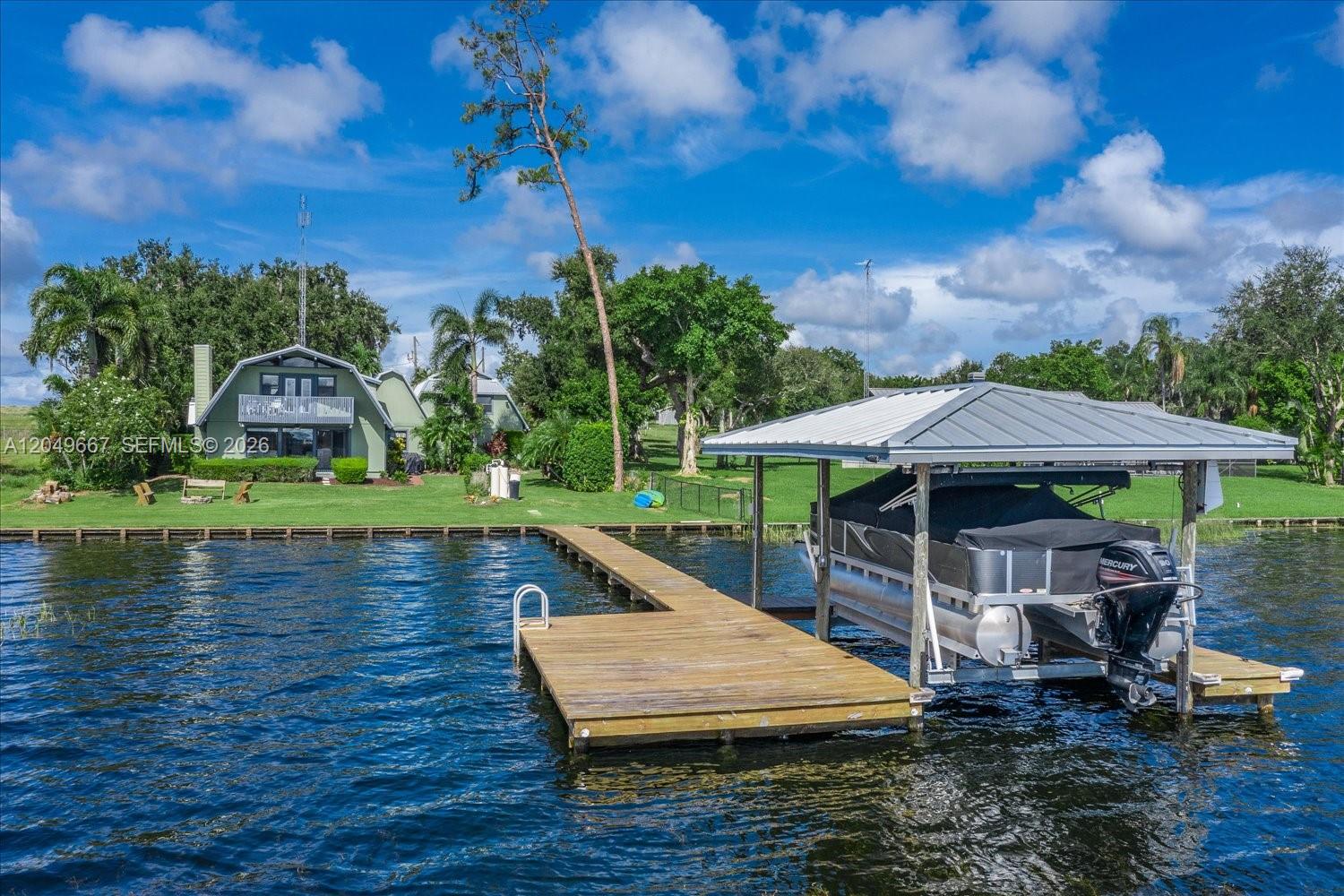 A wooden dock extends into a lake toward a house with a boat lift — 106 Wilmac Dr, Lake Placid FL 33852, LAKE PLACID, FL