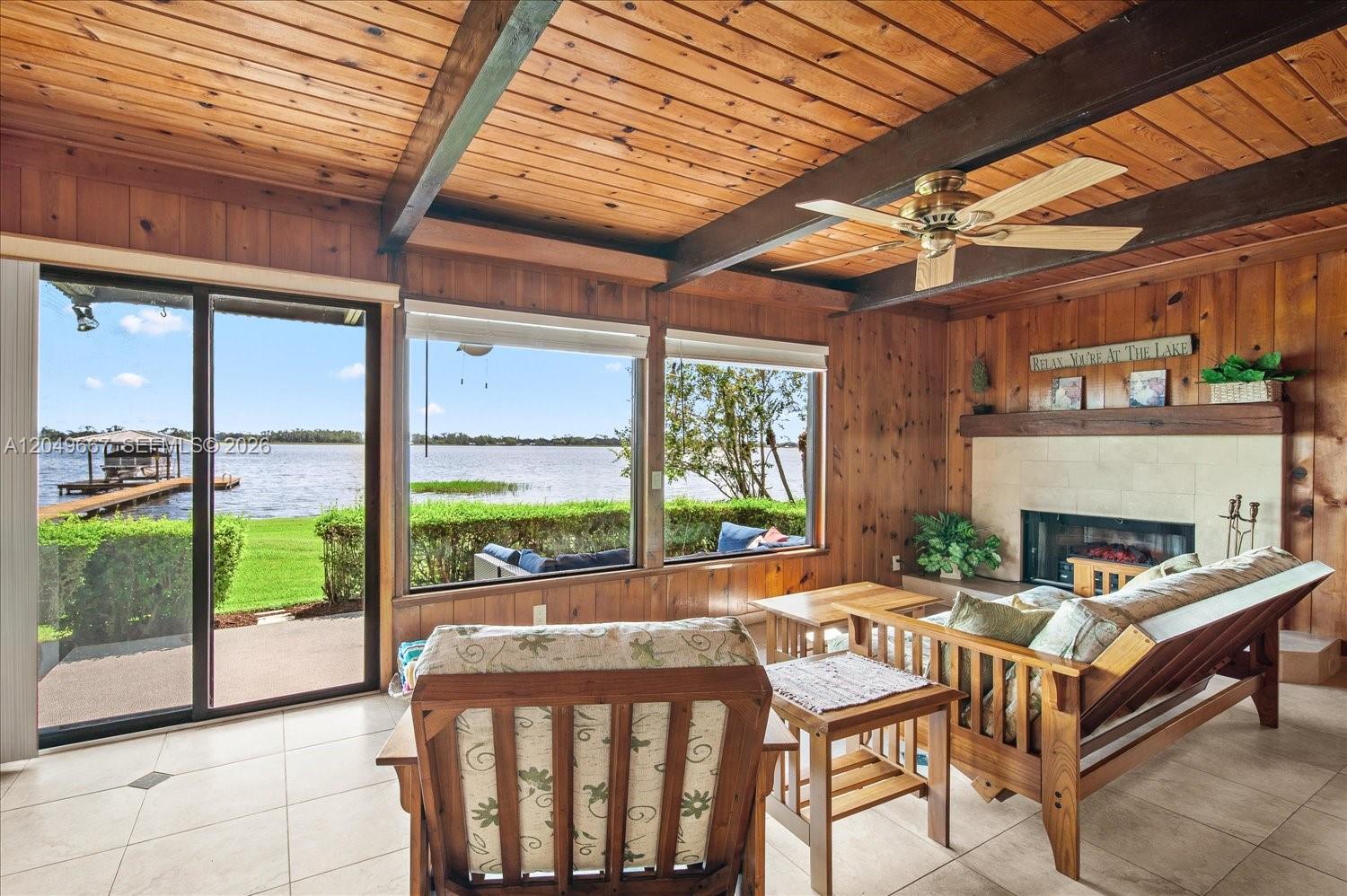 A living room with wood-paneled walls, a fireplace, and large windows overlooking a lake — 106 Wilmac Dr, Lake Placid FL 33852, LAKE PLACID, FL