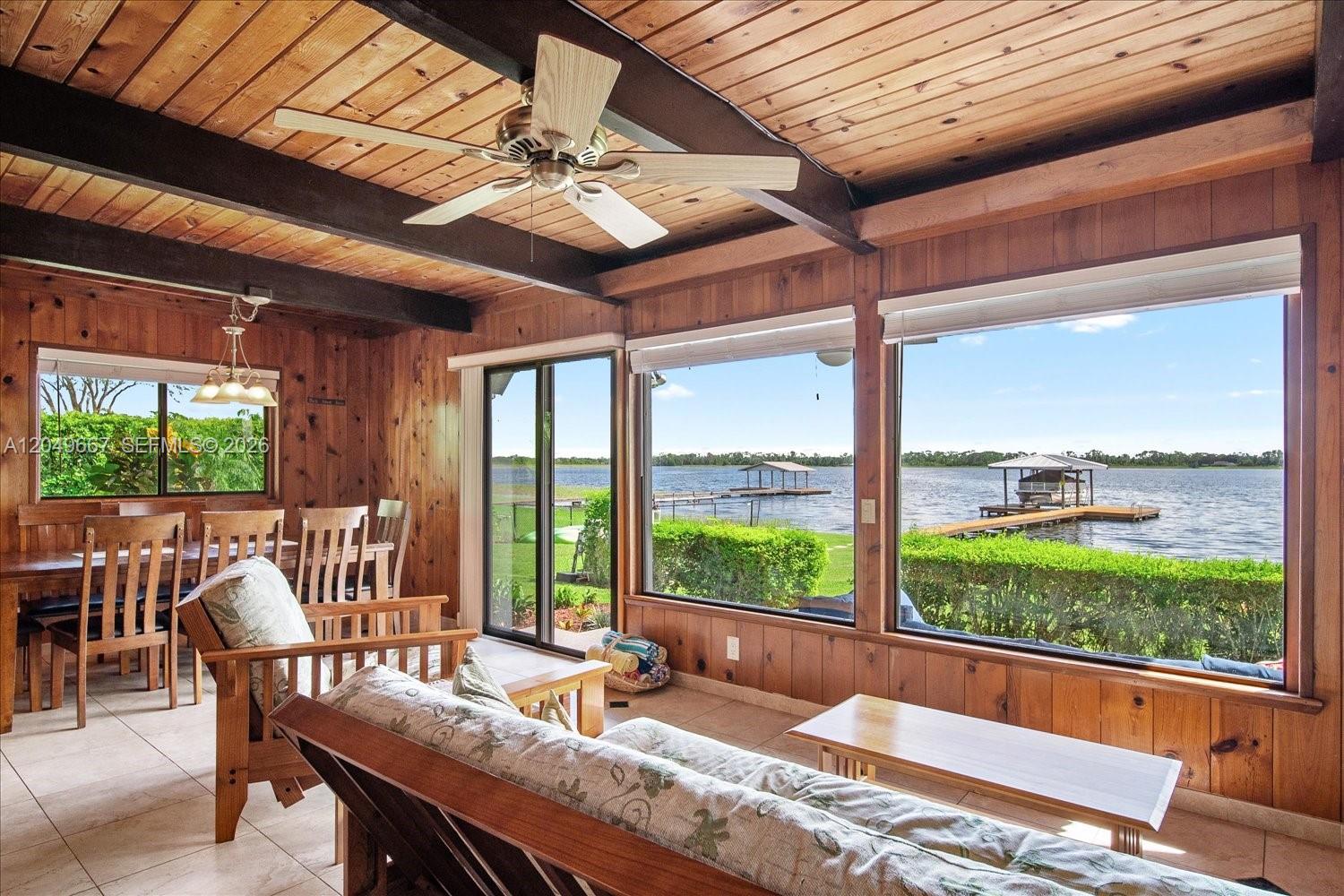 A wood-paneled living room features a ceiling fan and large windows overlooking a lake — 106 Wilmac Dr, Lake Placid FL 33852, LAKE PLACID, FL