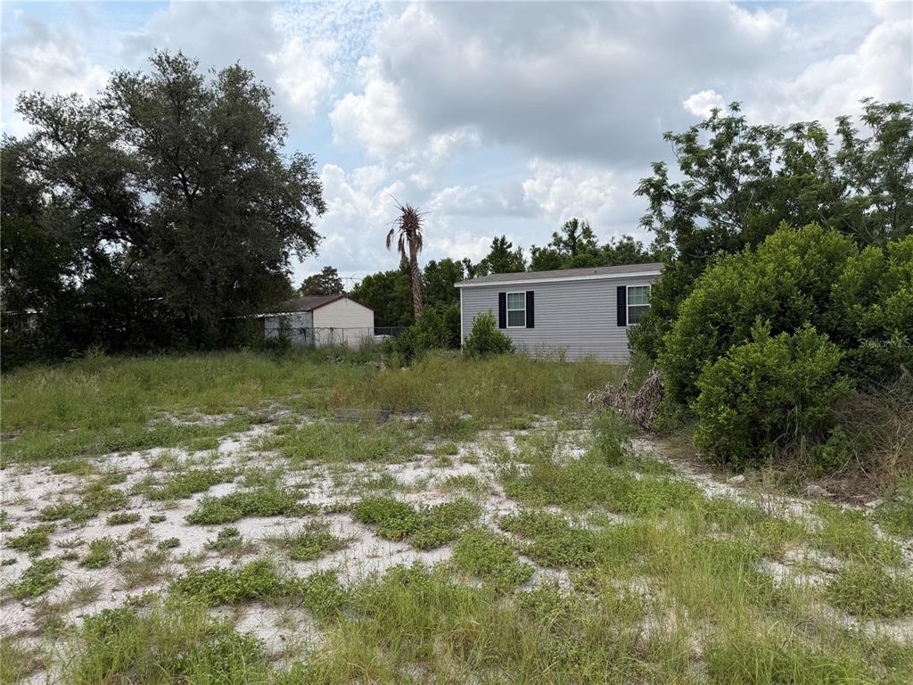 A gray mobile home sits on a grassy, sandy lot with trees and bushes — 2438 EDWIN STREET NE, WINTER HAVEN, FL