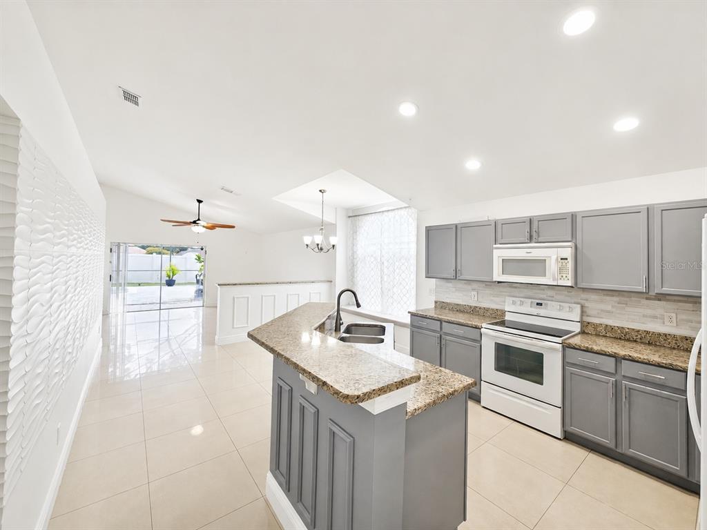 A kitchen with gray cabinets, granite countertops, and white appliances opens to a living area — 12786 MARIBOU CIRCLE, ORLANDO, FL