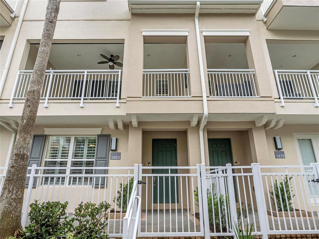 The exterior of a multi-story townhouse complex features white railings, green doors, and balconies — 1483 LAKE GEORGE DRIVE, LAKE MARY, FL