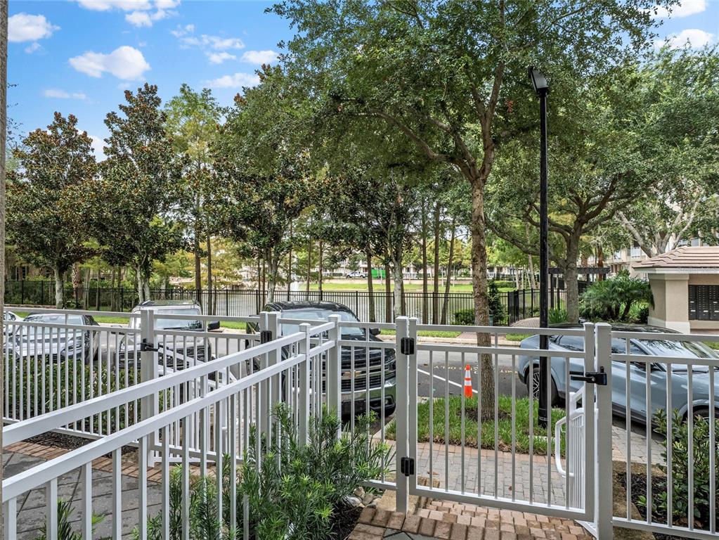 A white metal gate opens to a parking area with trees and a pond beyond — 1483 LAKE GEORGE DRIVE, LAKE MARY, FL