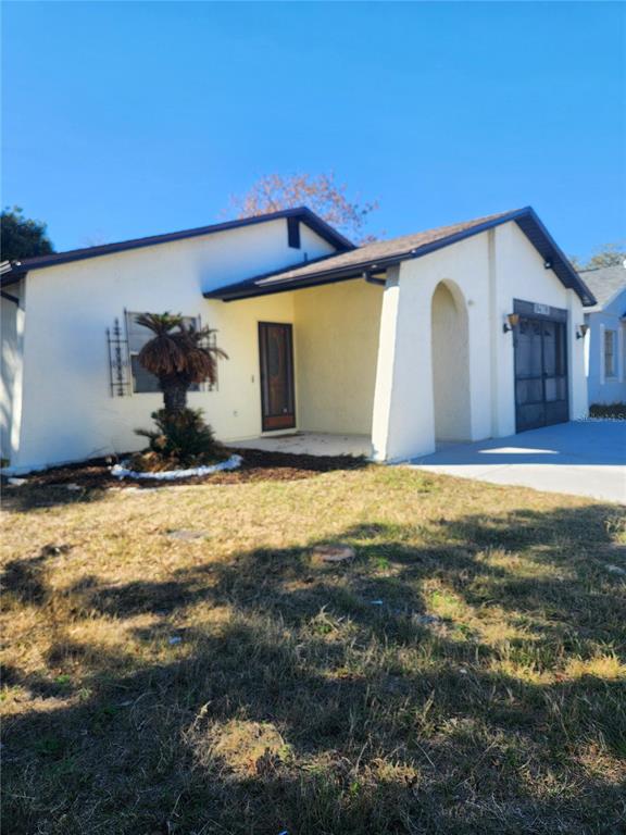 A single-story house with a stucco exterior, a covered entryway, and a screened garage door — 12813 KELLYWOOD CIRCLE, HUDSON, FL
