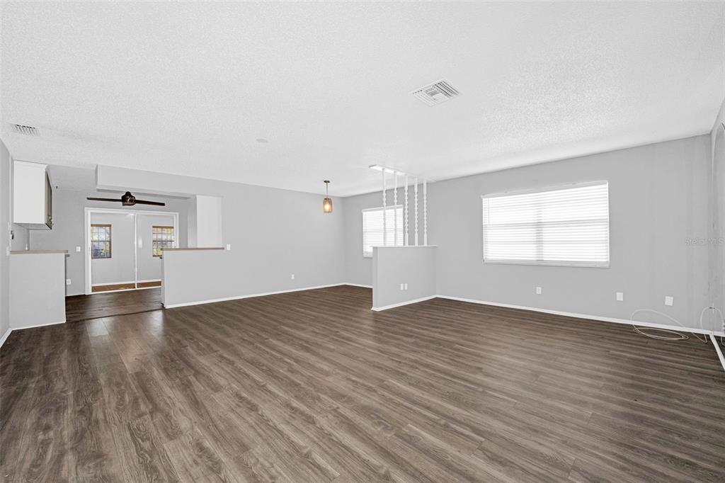 An open-concept living and dining area features gray walls, wood-look flooring, and white trim — 12813 KELLYWOOD CIRCLE, HUDSON, FL