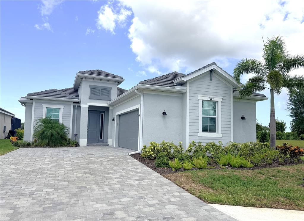 A light gray single-story house with a paver driveway, a two-car garage, and a palm tree — 17697 SANTORINI COURT, VENICE, FL