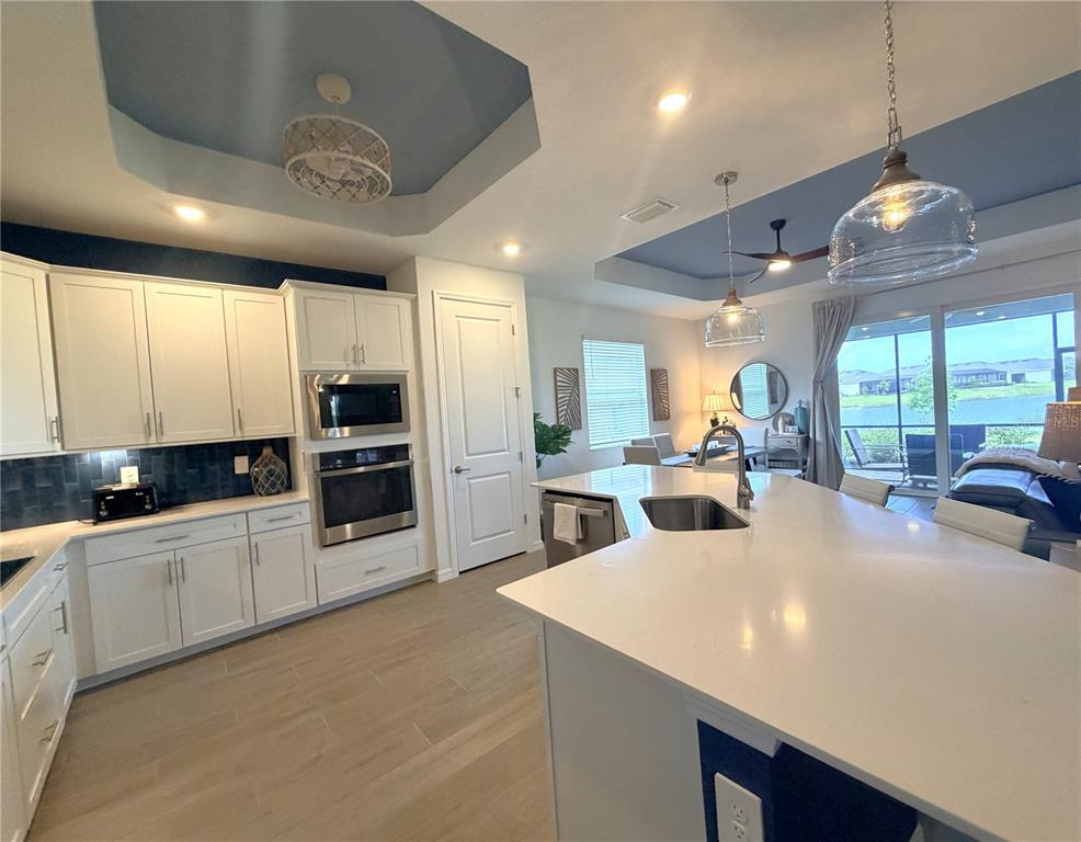 A modern kitchen features white cabinetry, a large island with a sink, and blue tray ceilings — 17697 SANTORINI COURT, VENICE, FL