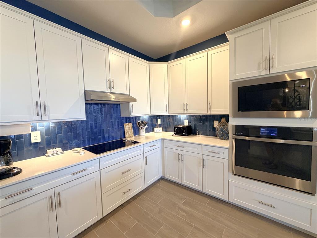 A kitchen features white cabinets, blue tile backsplash, stainless steel appliances, and light countertops — 17697 SANTORINI COURT, VENICE, FL