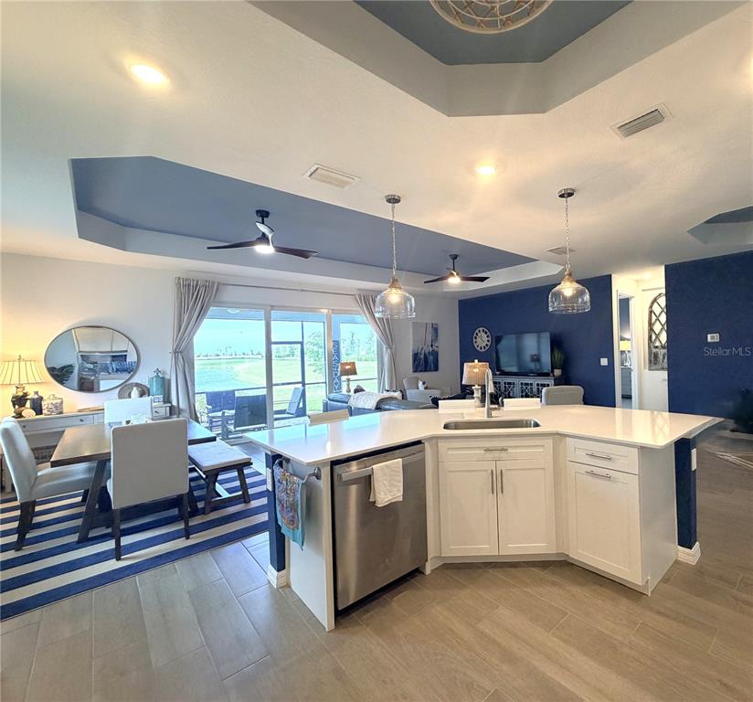 A kitchen with a white island and stainless steel dishwasher overlooks a dining and living area — 17697 SANTORINI COURT, VENICE, FL