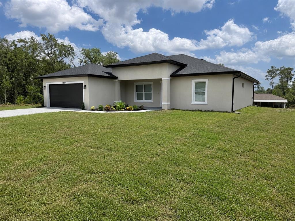 A single-story house with a dark garage door, beige stucco exterior, and a grassy lawn — 17229 SW 42ND TERRACE, OCALA, FL