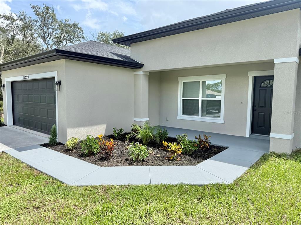 The exterior of a single-story house features a gray garage door, a front entrance, and landscaping — 17229 SW 42ND TERRACE, OCALA, FL