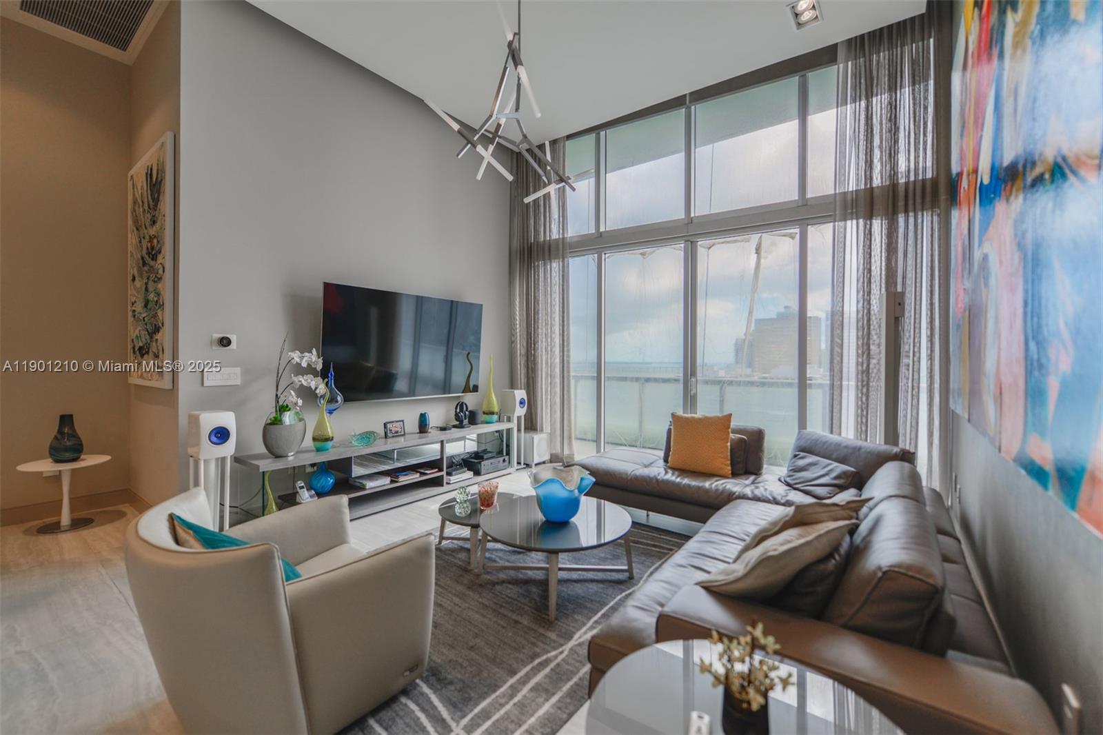 A modern living room features a large television, leather sofa, and floor-to-ceiling windows — 495 Brickell Ave # 2211, Miami FL 33131, MIAMI, FL