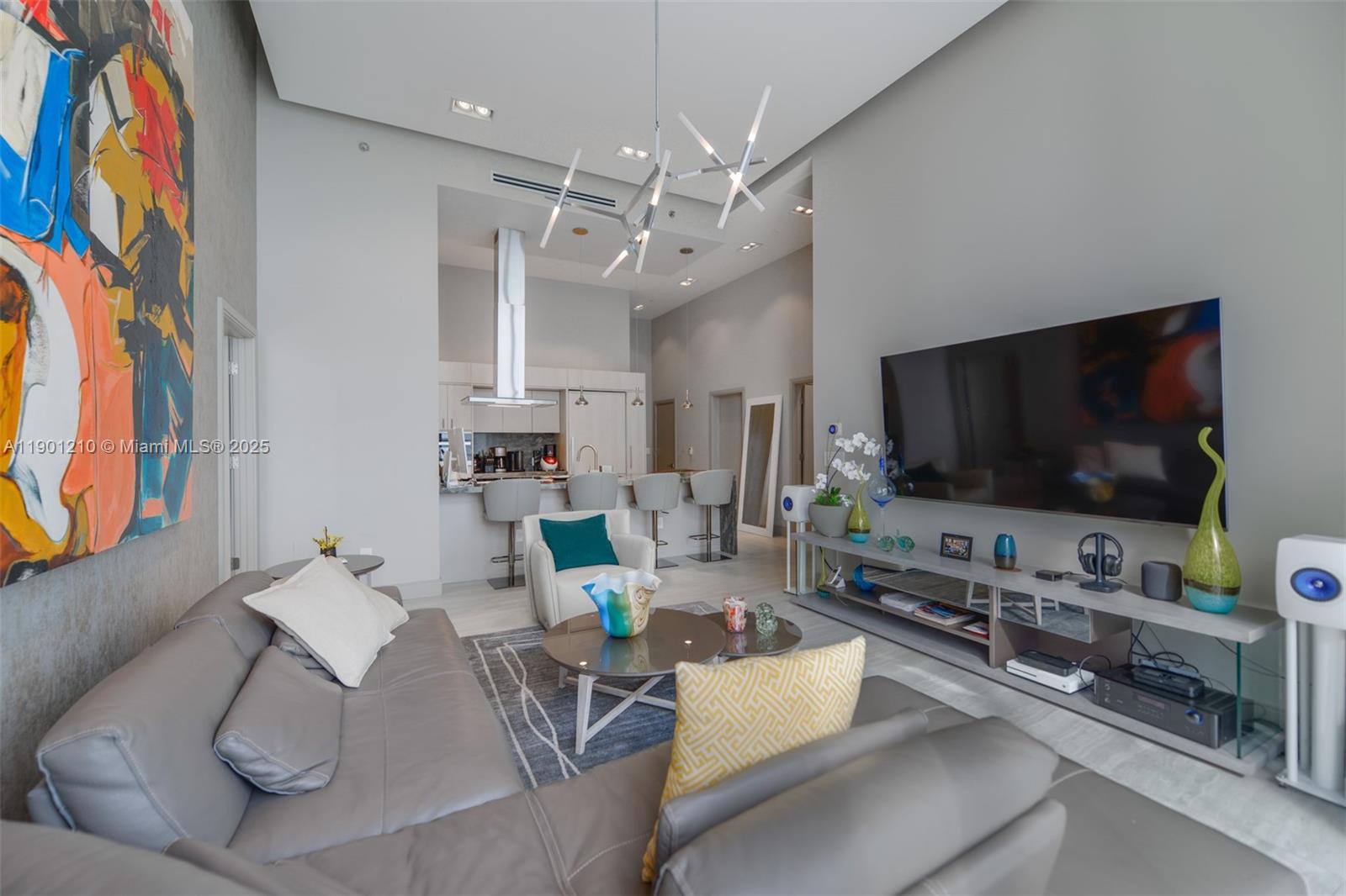 A modern living room features a grey sectional sofa, a large abstract painting, and kitchen — 495 Brickell Ave # 2211, Miami FL 33131, MIAMI, FL