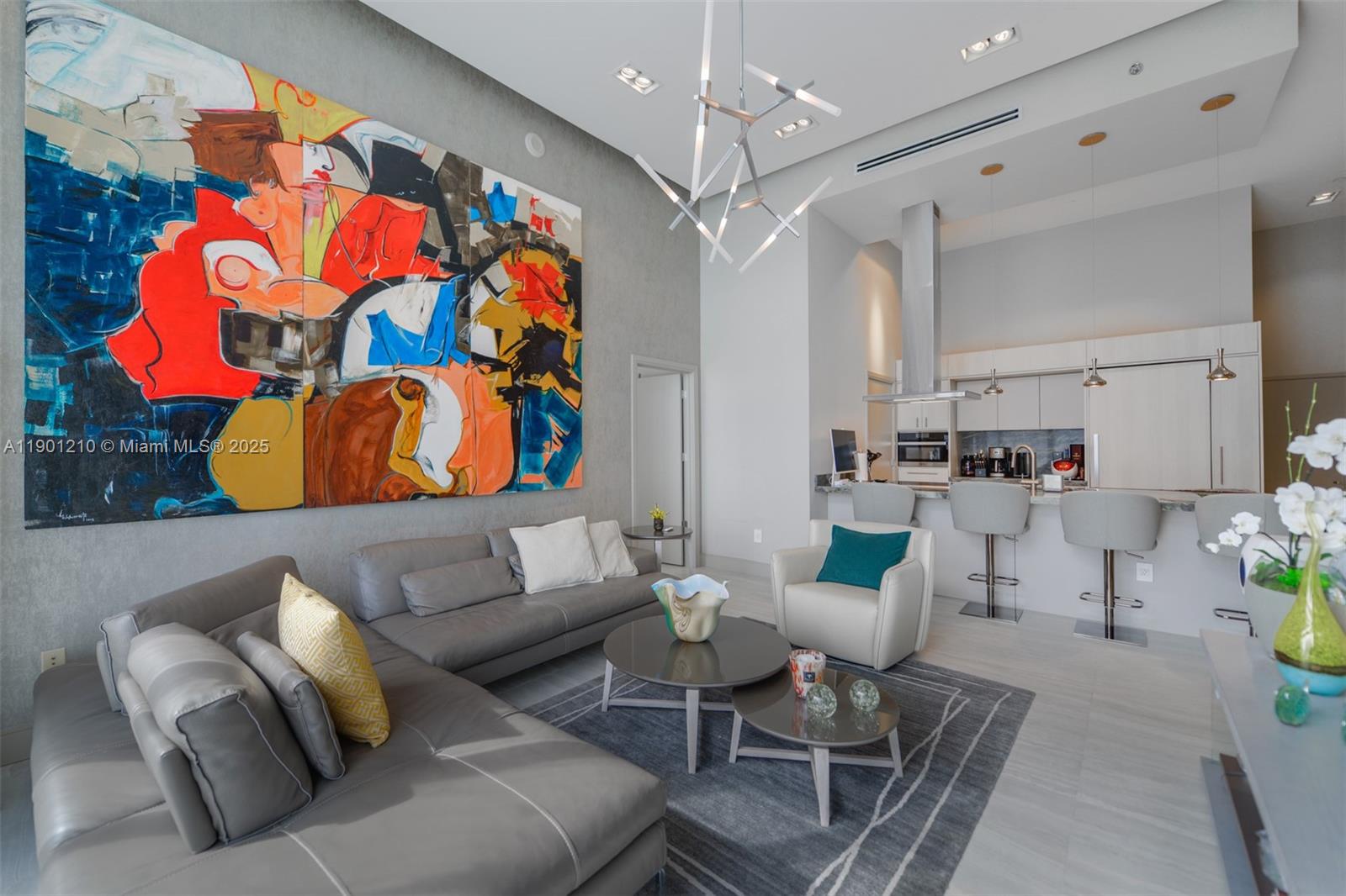 A modern living room features a large abstract painting, gray sectional sofa, and open kitchen — 495 Brickell Ave # 2211, Miami FL 33131, MIAMI, FL