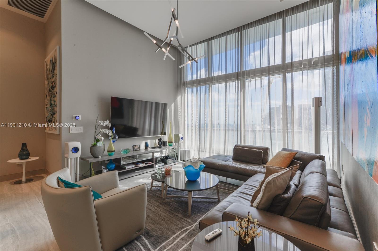 A modern living room features a large sectional sofa, floor-to-ceiling windows, and a sculptural chandelier — 495 Brickell Ave # 2211, Miami FL 33131, MIAMI, FL
