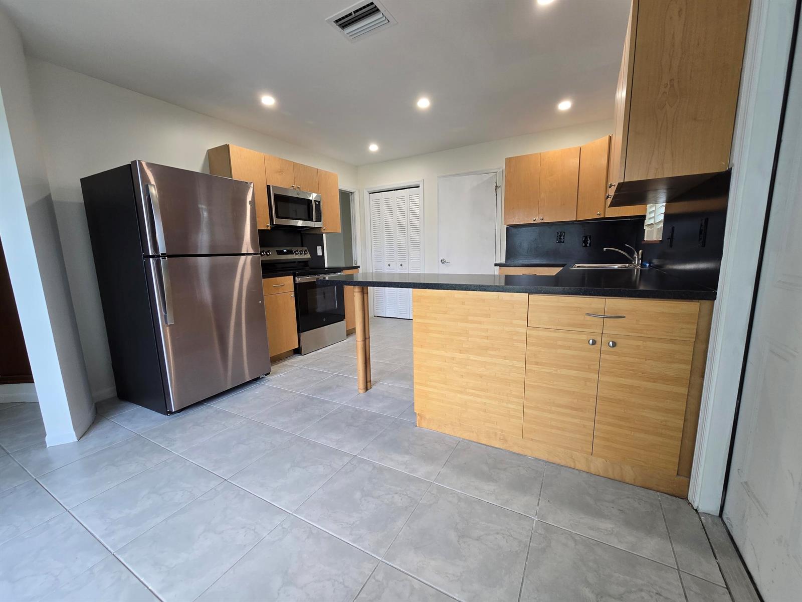 A kitchen features light wood cabinets, black countertops, stainless steel appliances, and gray tile flooring — 800 Ibis Way # 1, North Palm Beach FL 33408, NORTH PALM BEACH, FL
