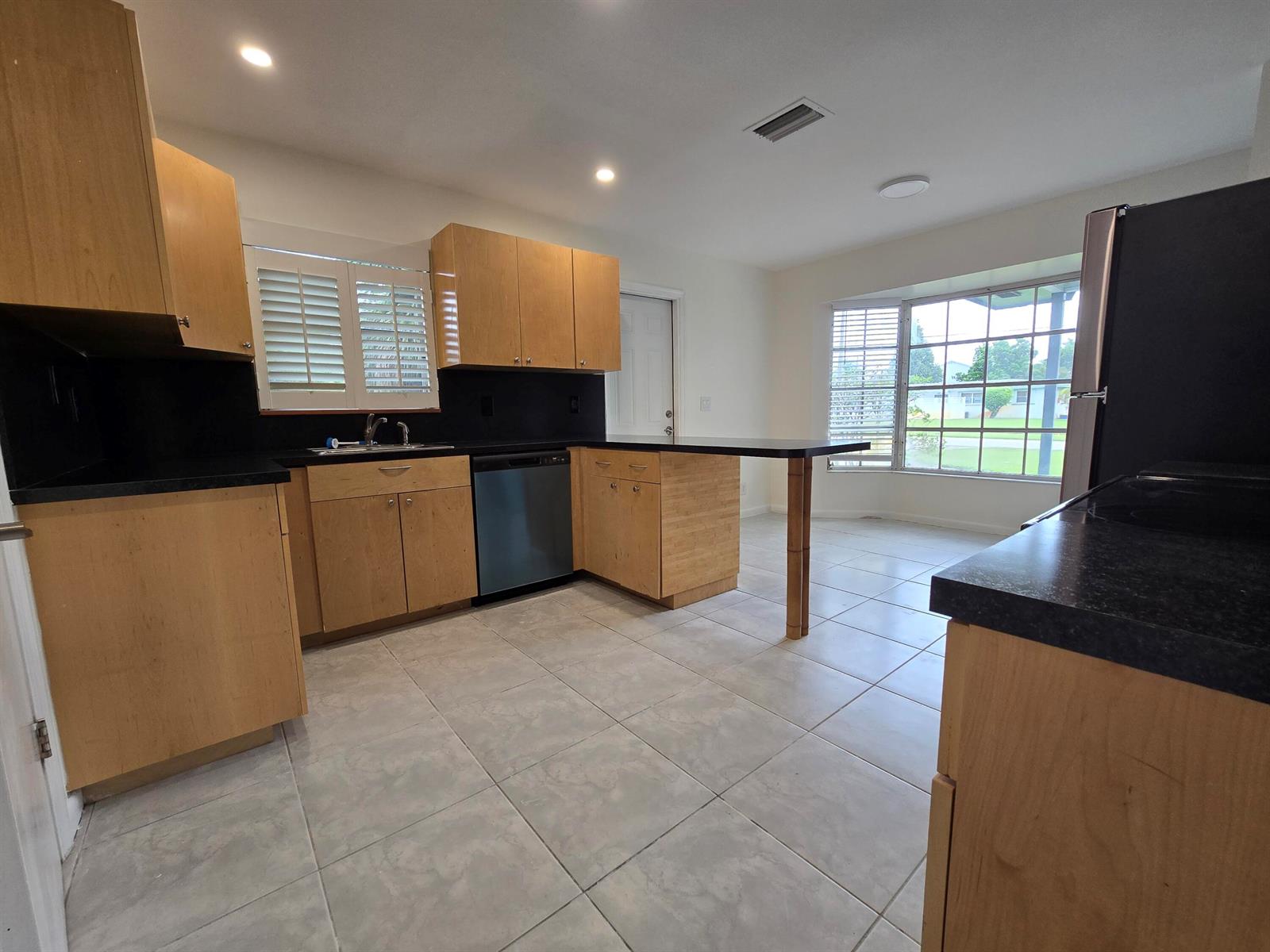 A kitchen features light wood cabinets, black countertops, a dishwasher, and large floor tiles — 800 Ibis Way # 1, North Palm Beach FL 33408, NORTH PALM BEACH, FL