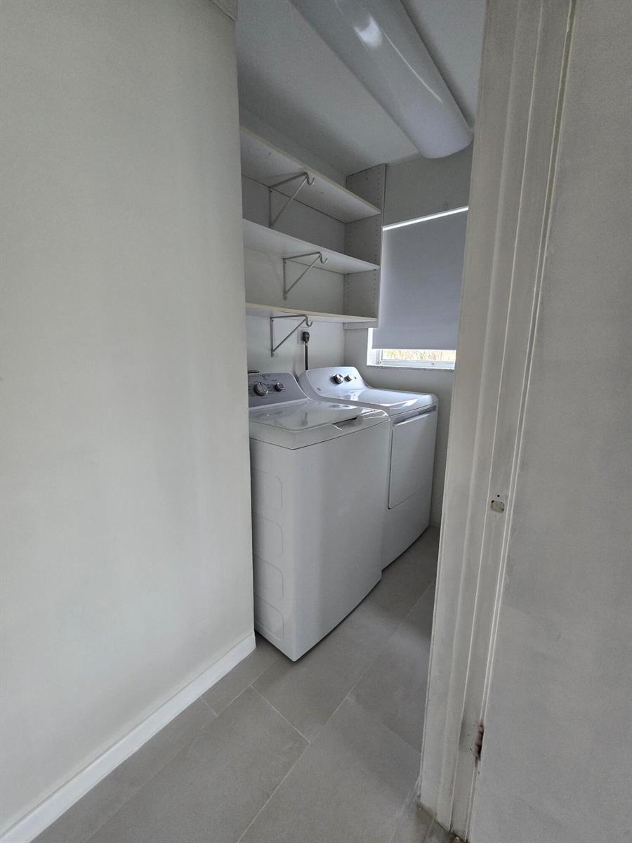 A laundry room features a white washer and dryer beneath open shelving and a window — 800 Ibis Way # 1, North Palm Beach FL 33408, NORTH PALM BEACH, FL