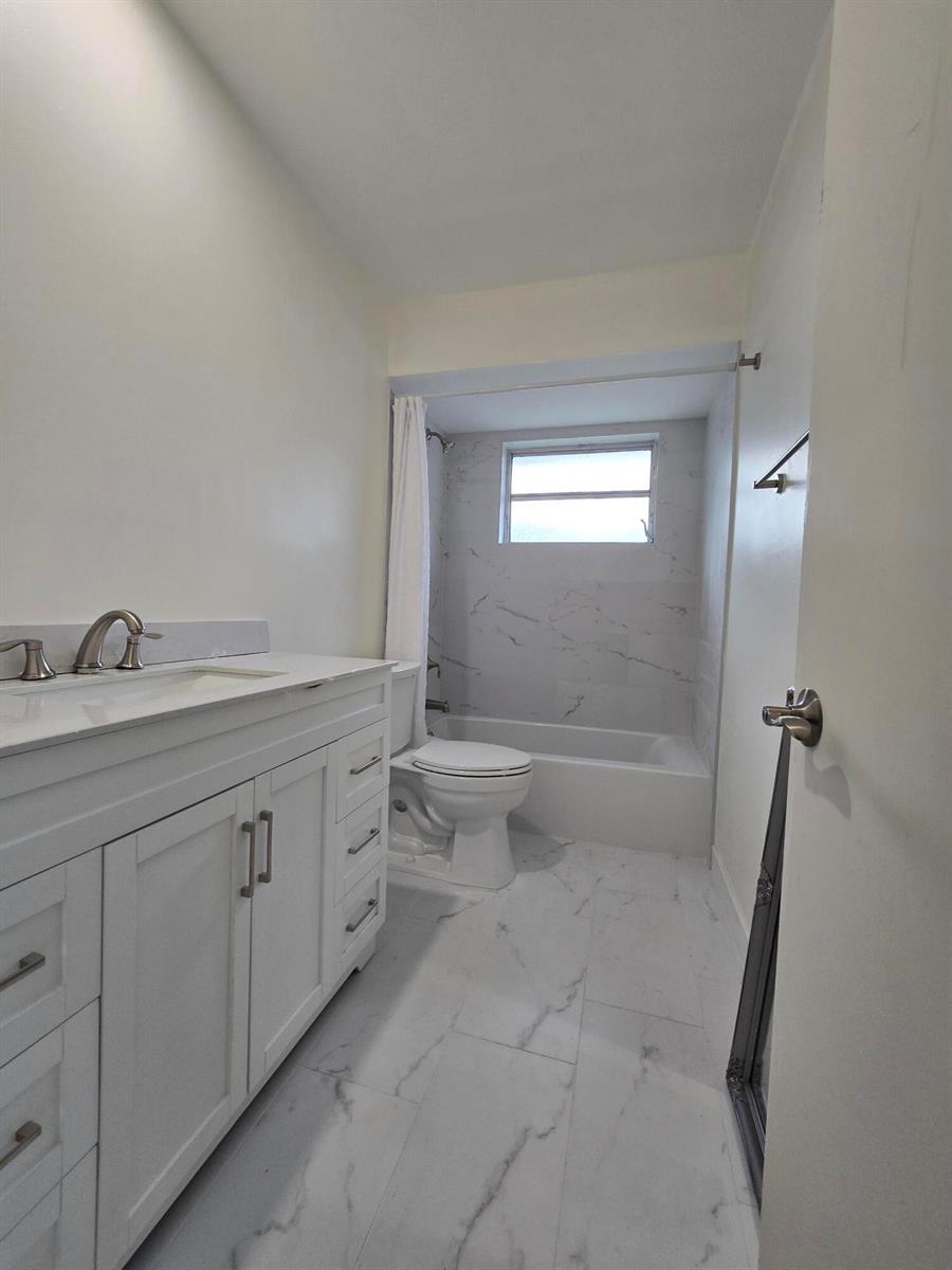 A bathroom features a white vanity, a toilet, and a bathtub with marble-look tile — 800 Ibis Way # 1, North Palm Beach FL 33408, NORTH PALM BEACH, FL