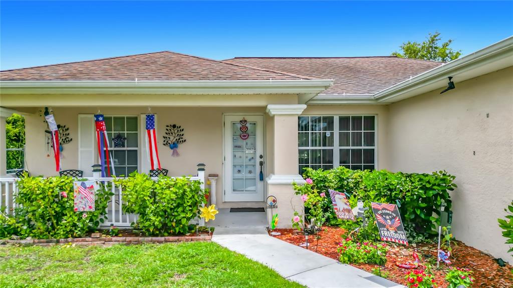 The exterior of a single-story house features a front porch, landscaping, and patriotic decorations — 2903 38TH STREET SW, LEHIGH ACRES, FL