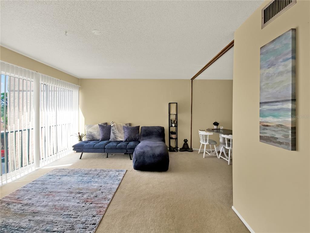 A living room features a blue sectional sofa, a rug, and a small dining area — 2763 WOODGATE LANE UNIT 307, SARASOTA, FL