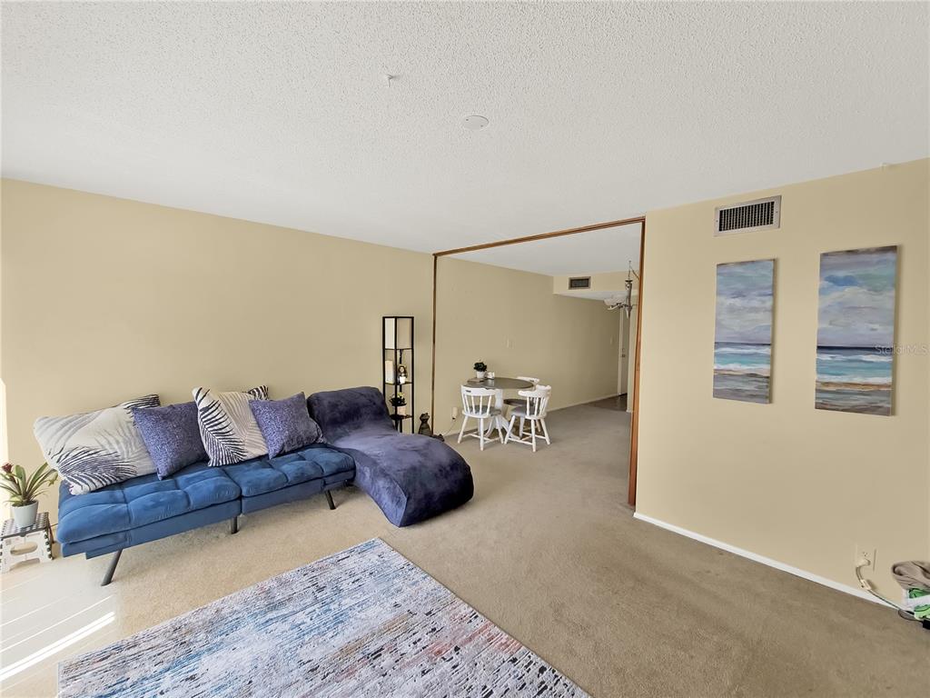 A living room with a blue sectional sofa, a patterned rug, and a dining area — 2763 WOODGATE LANE UNIT 307, SARASOTA, FL