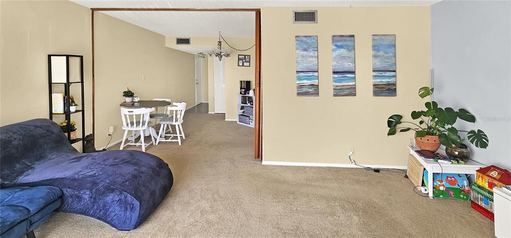 A living room with beige carpet, a blue chaise lounge, and a dining area beyond — 2763 WOODGATE LANE UNIT 307, SARASOTA, FL